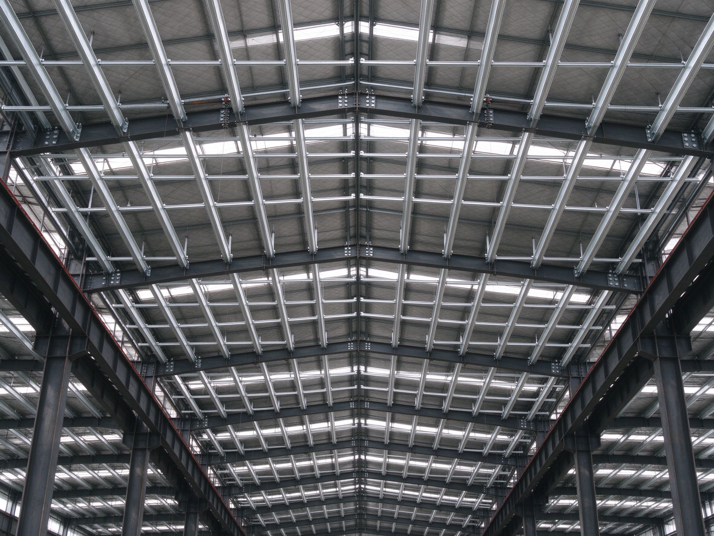 Upward view inside a steel roof structure, C/Z purlins resting on roof frames that carry loads down to the columns (illustrative concept image)